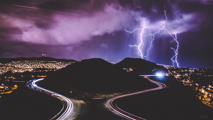 Lightning strikes over a city at night with light trails on a road