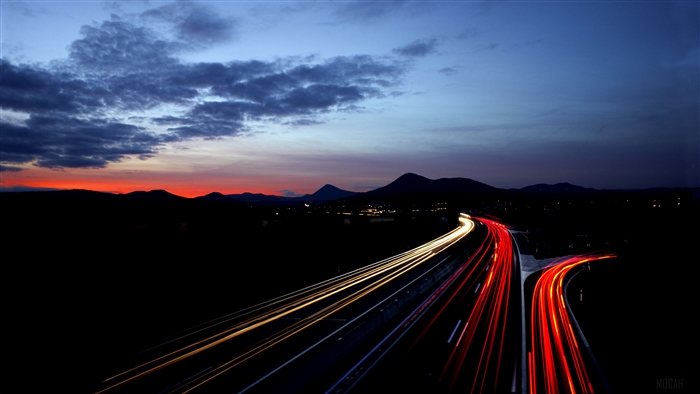 Highway light trails at dusk with mountains