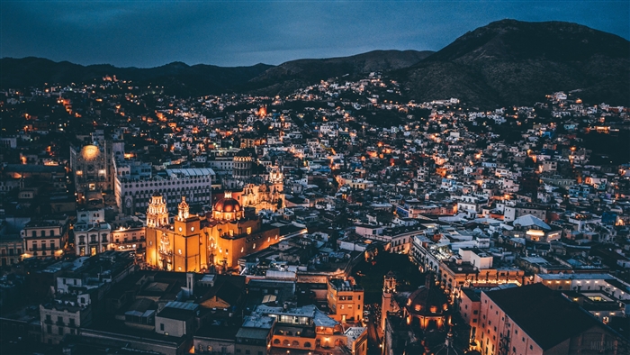 Night city view with illuminated buildings and mountains