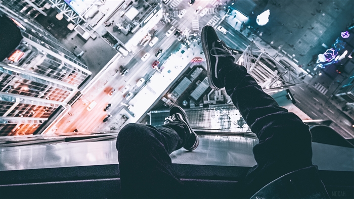 Man sitting on skyscraper edge overlooking city at night 4K