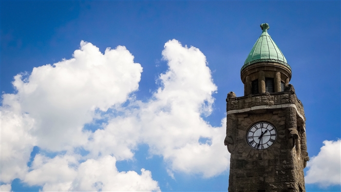Stone tower with clock and green dome against blue sky with clouds