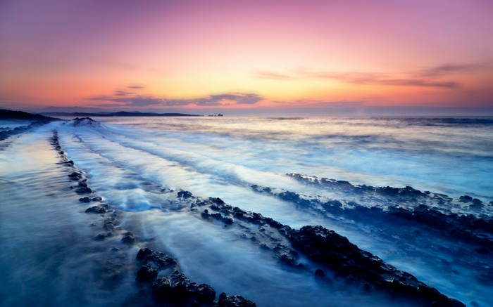 Ocean waves crashing on rocky shore at sunset