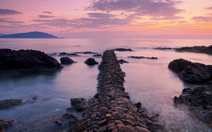 Stone path leading into the ocean at sunset