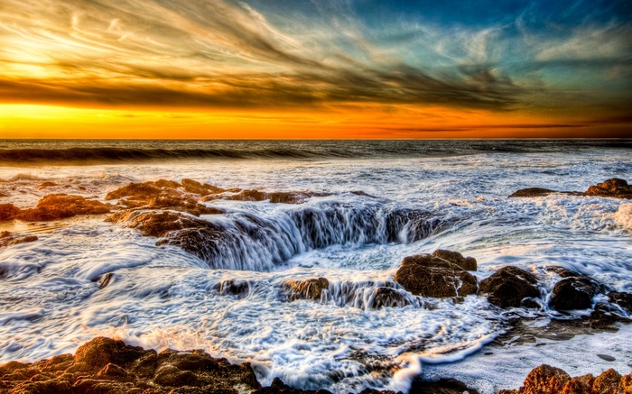 Ocean waves crashing into rocky shore at sunset
