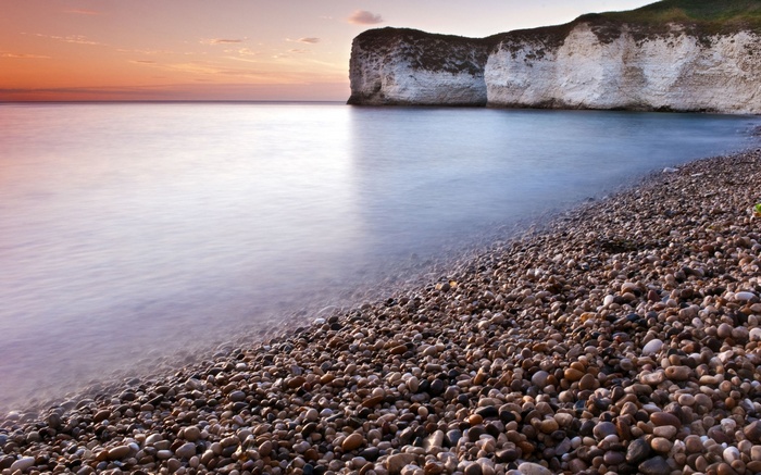 Pebble beach with white cliffs and calm sea at sunset