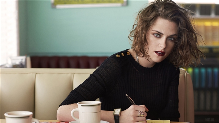 Kristen Stewart in a black top writing at a diner
