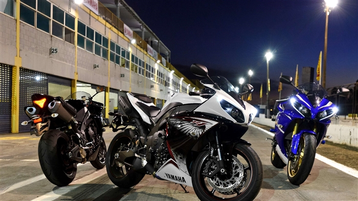 Three Yamaha R1 motorcycles on a race track at night