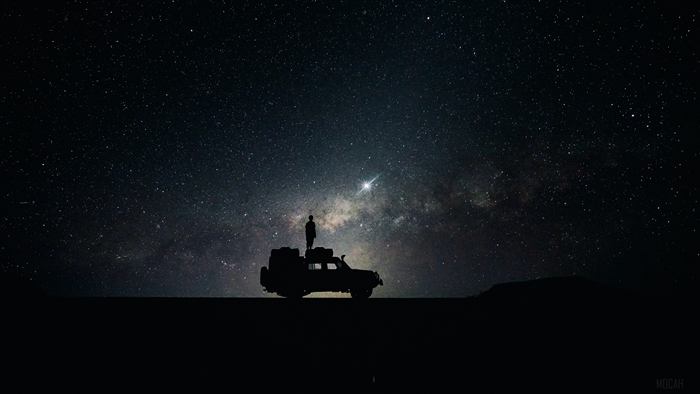 Silhouette of a person on a car under the stars