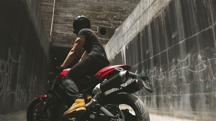 Motorcyclist in helmet on red motorcycle near concrete wall