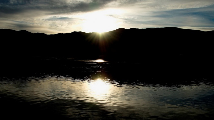Sunset over a dark mountain range and water