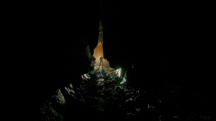 Man standing in a dark cave with light ahead 4K