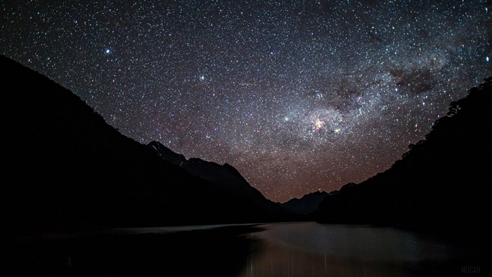 Starry night sky over mountains and lake