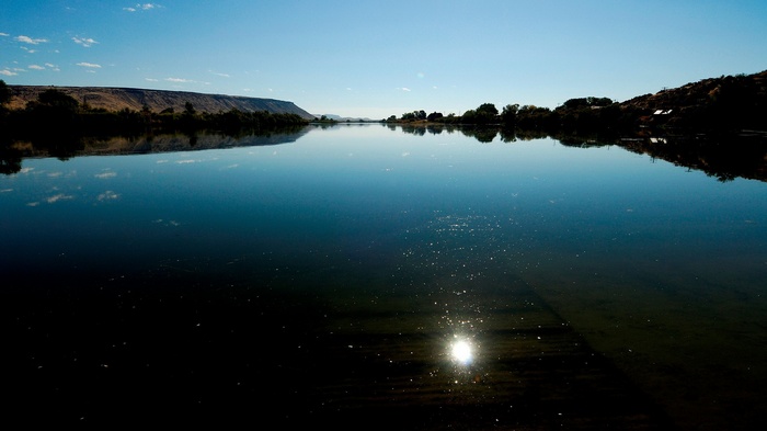 Calm river reflecting a clear blue sky and distant hills