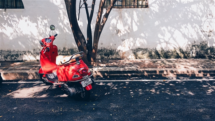 Red scooter parked on a street with tree shadows