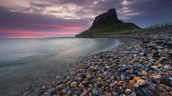 Lindisfarne Castle on a rocky shore at sunset