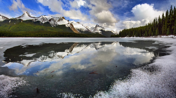 Snow-capped mountains reflected in a partially frozen lake