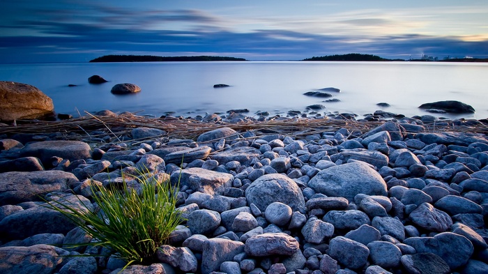 Rocky shore with calm water and distant islands at dusk