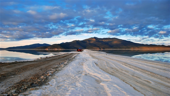 Red vehicle on salt desert road with mountains