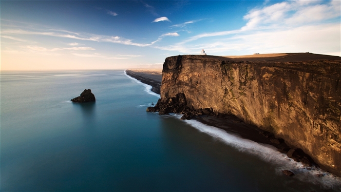 Person on cliff overlooking black sand beach and ocean