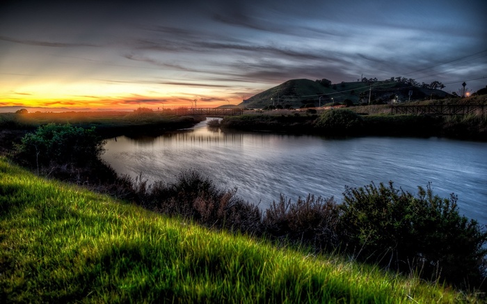Sunset over a river with a bridge and hill