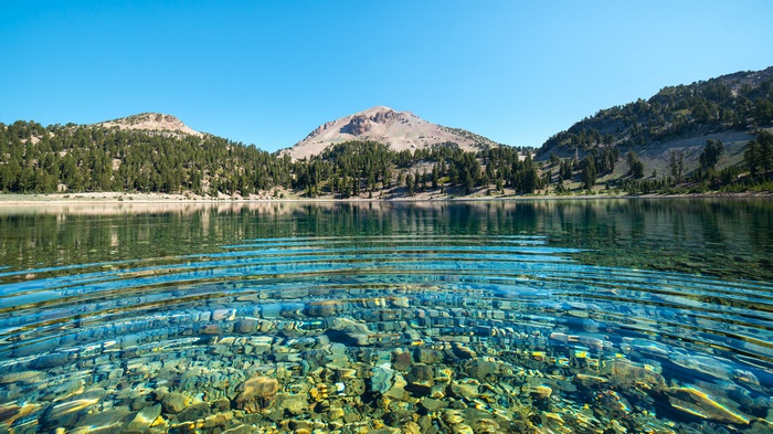 Clear lake with rocky bottom and forested mountains