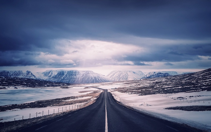 Road through snowy mountains under cloudy sky