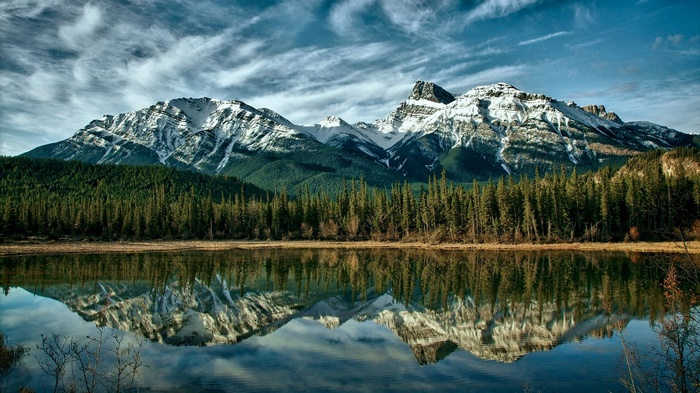 Snow-capped mountains reflected in a lake with pine forest