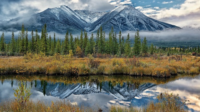 Snow-capped mountains reflected in a calm lake with pine trees