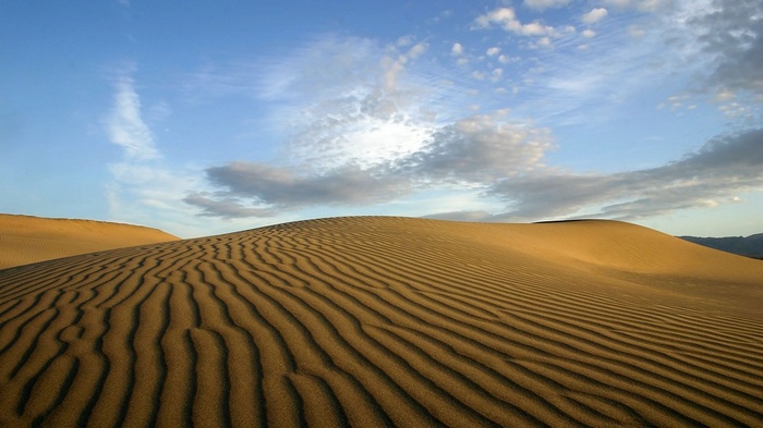 Sand dunes with rippled patterns under a cloudy sky