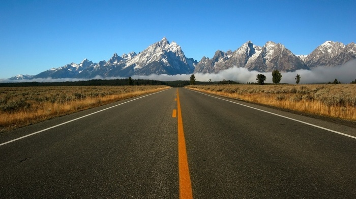 Road leading to snow-capped mountains and clouds