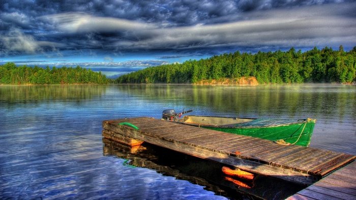 Wooden dock with green boat on a misty lake
