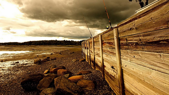 Fishing rods on a wooden pier by a muddy shore
