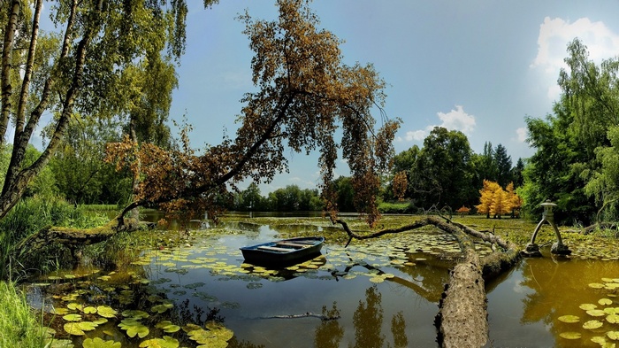 Boat on a lily pad covered pond with trees and a stone lantern