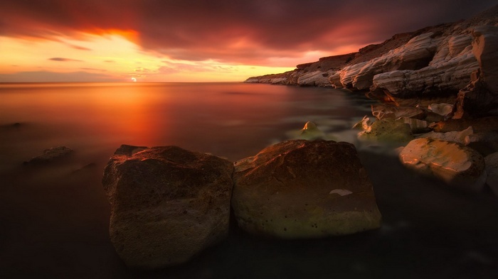 Sunset over rocky coastline with calm sea
