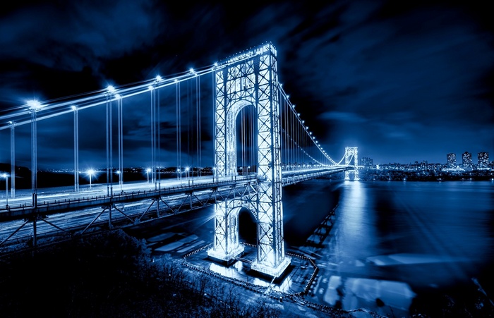 Illuminated Suspension Bridge Over Calm River At Night