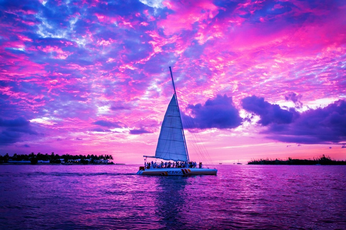 Catamaran sailing on purple ocean during pink and purple sunset