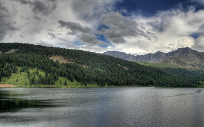 Lake and forested mountains under cloudy sky