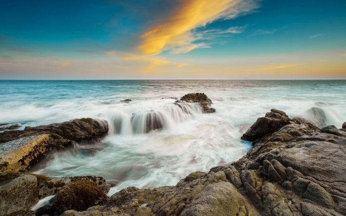 Ocean waves crashing on rocky shore at sunset