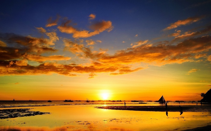 Sunset over a beach with boats and people