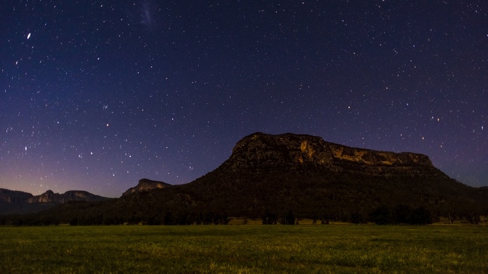 Starry night sky over mountains and a field