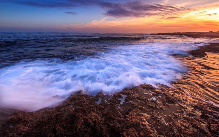 Ocean waves crashing on rocky shore at sunset