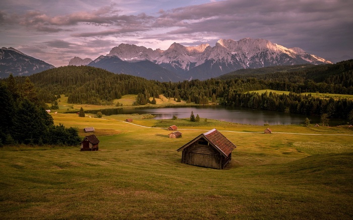 Wooden cabins by a lake with mountains in the background