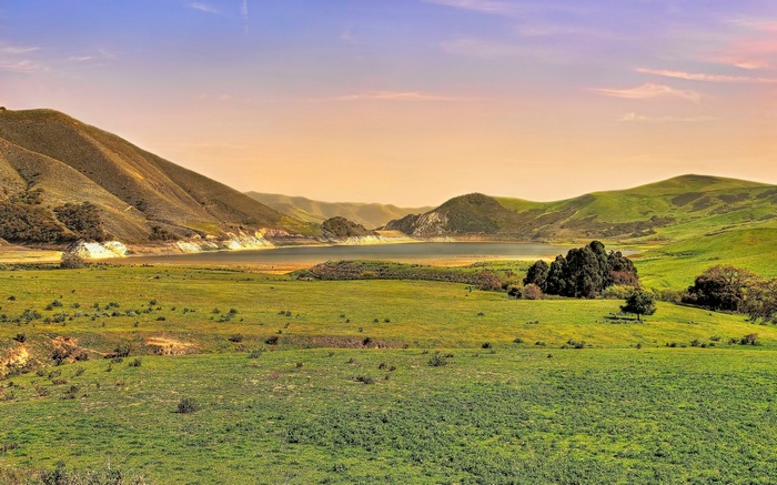 Rolling green hills and a lake under a sunset sky