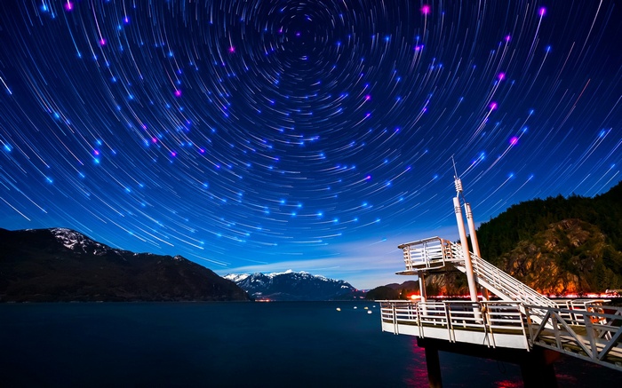 Star trails over a lake and mountains