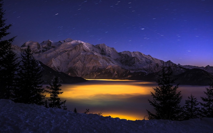 Snowy mountains under starry night sky with glowing fog