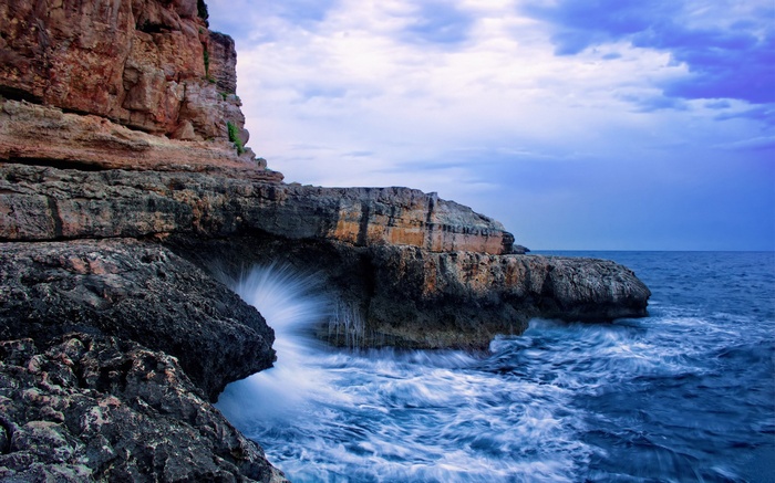 Waves crashing against rocky cliffs under a cloudy sky