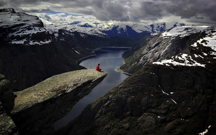 Person sitting on Trolltunga rock overlooking a fjord in Norway