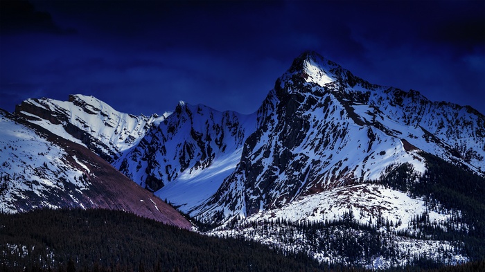 Snow-covered mountains under a dark blue sky
