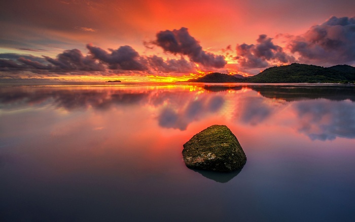 Sunset over a calm ocean with a rock