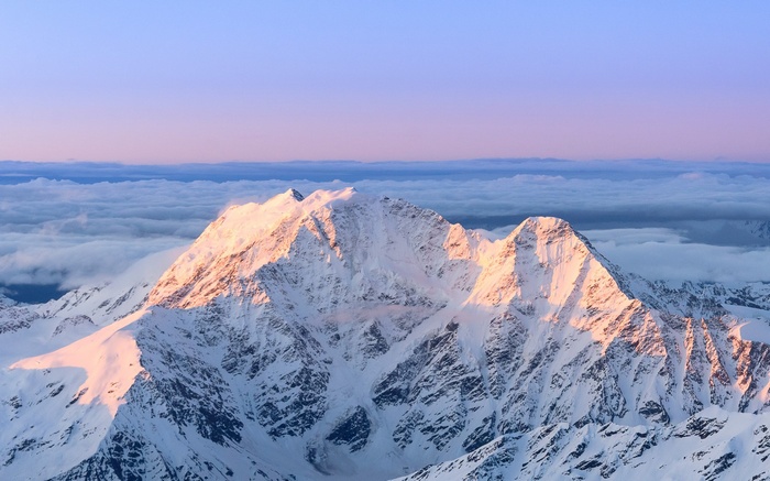 Snow-covered mountains at sunrise above clouds